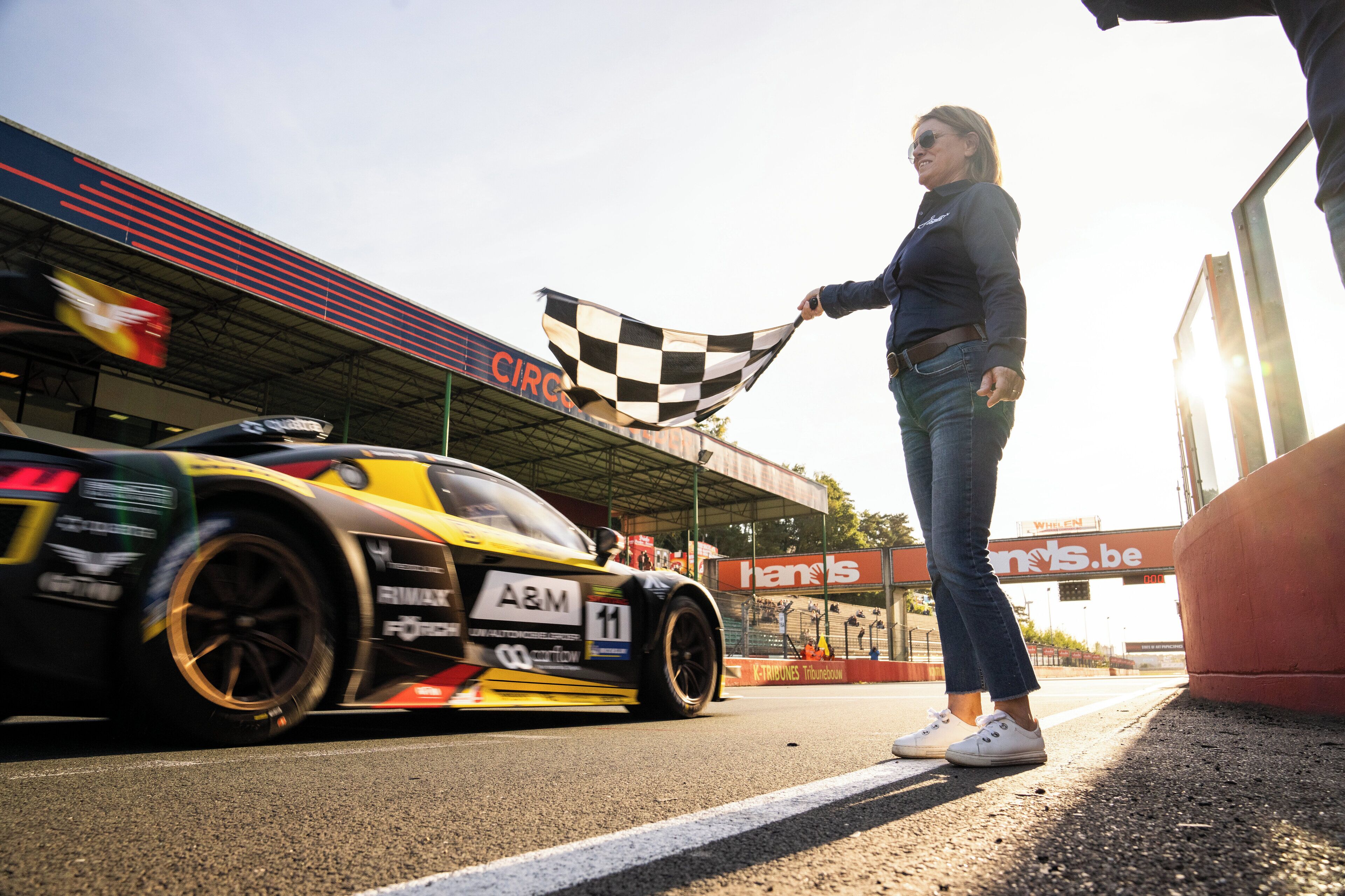 A race car parked at a trackside area with a checkered flag being held by a person.
