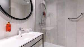 A modern bathroom with a white sink, a large mirror, a handheld showerhead, and a glass-enclosed shower.