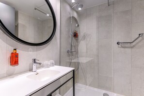 A modern bathroom with a white sink, a large mirror, a handheld showerhead, and a glass-enclosed shower.