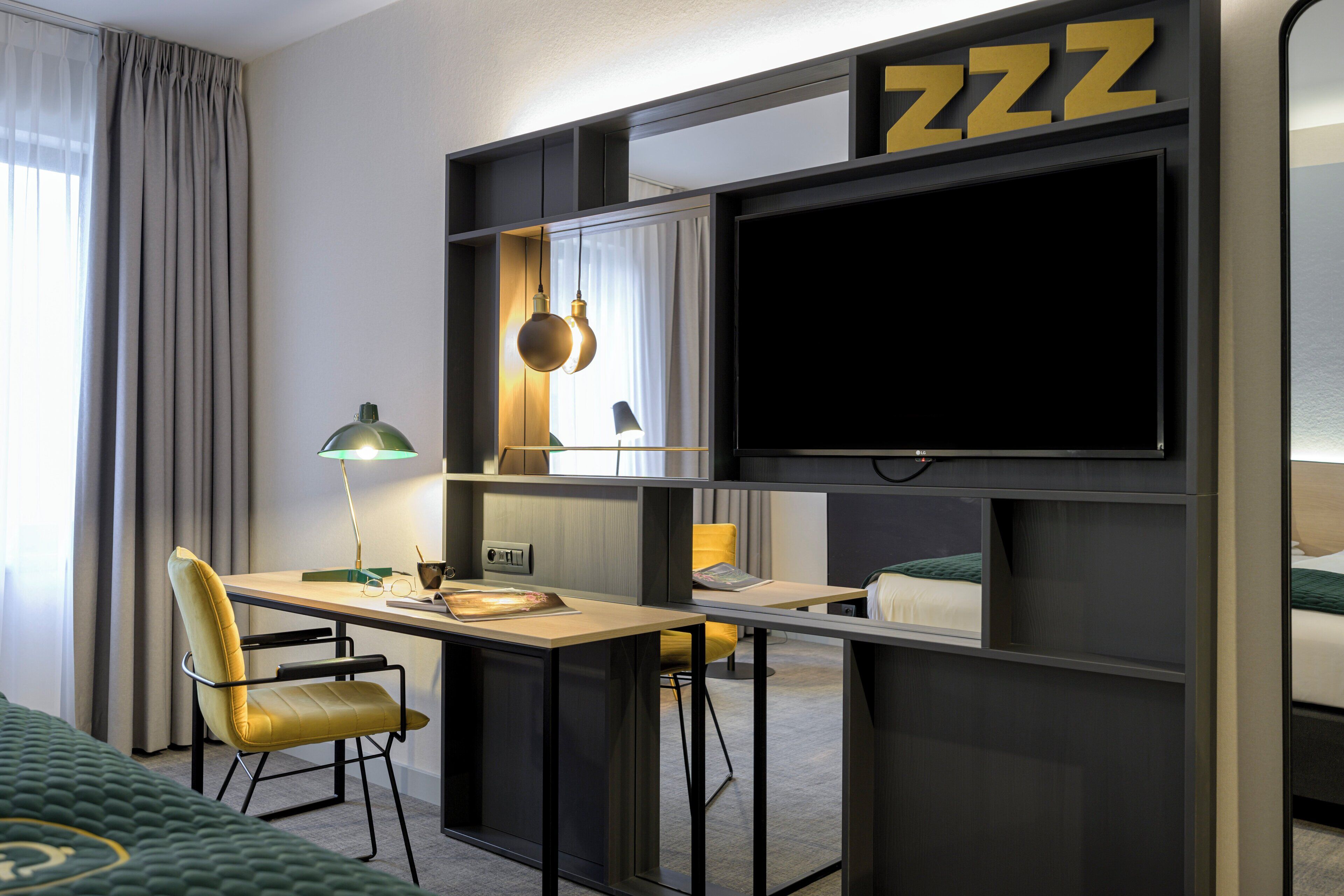 A modern hotel room with a desk, chair, TV, and a bed.