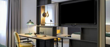 A modern hotel room with a desk, chair, TV, and a bed.