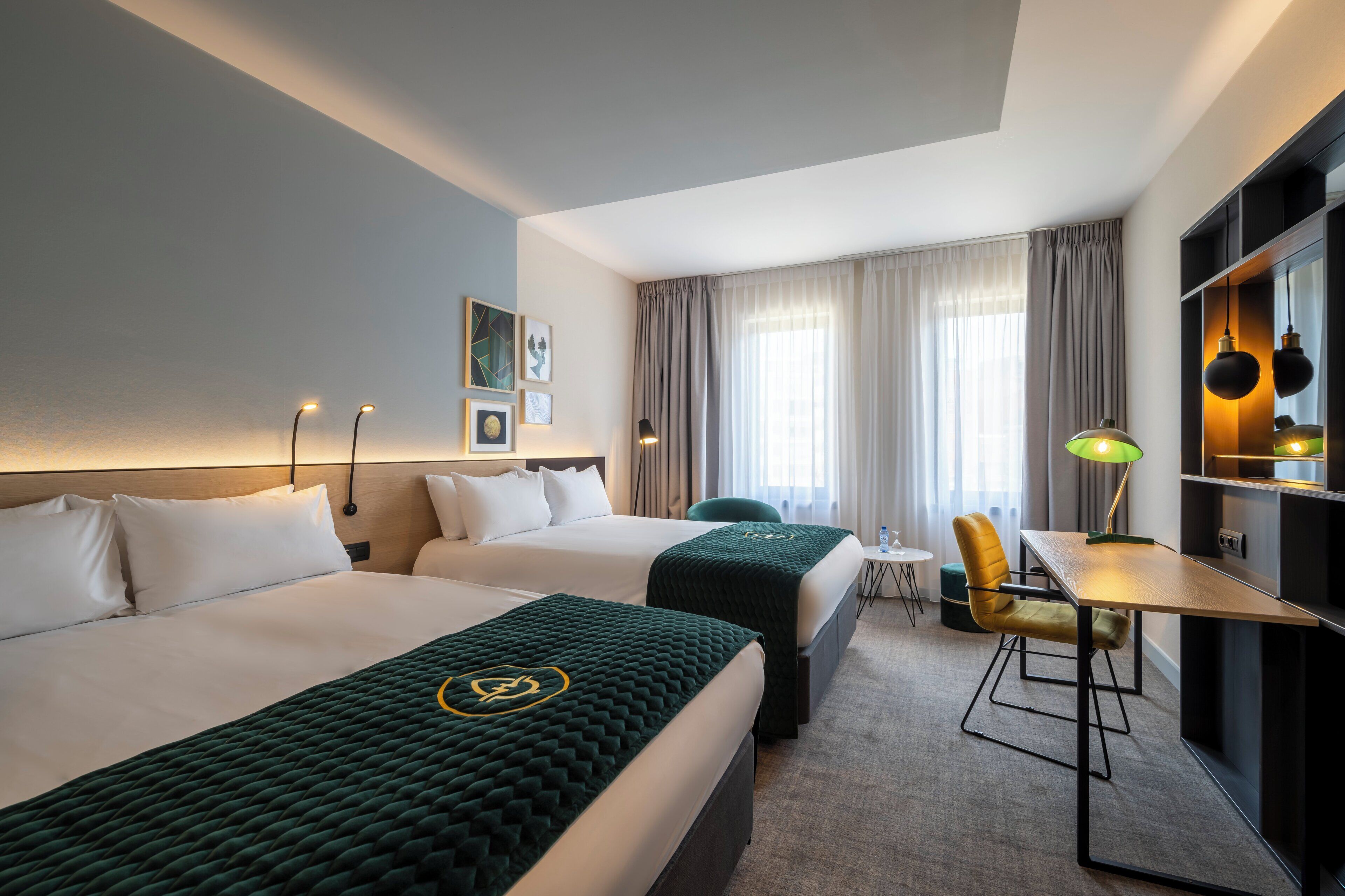 A hotel room with two beds, a desk, a chair, a lamp, and a TV.