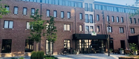 A multi-story hotel with a brick facade, large windows, and a covered entrance area with seating and bicycles.