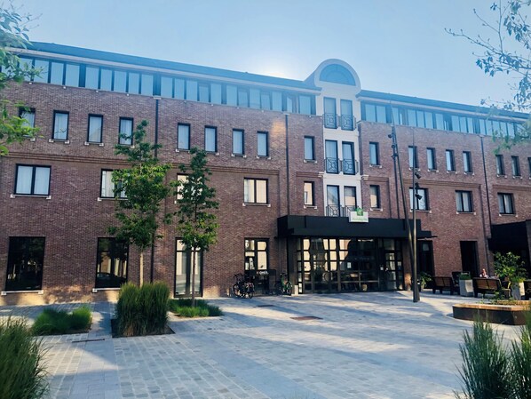 A multi-story hotel with a brick facade, large windows, and a covered entrance area with seating and bicycles.