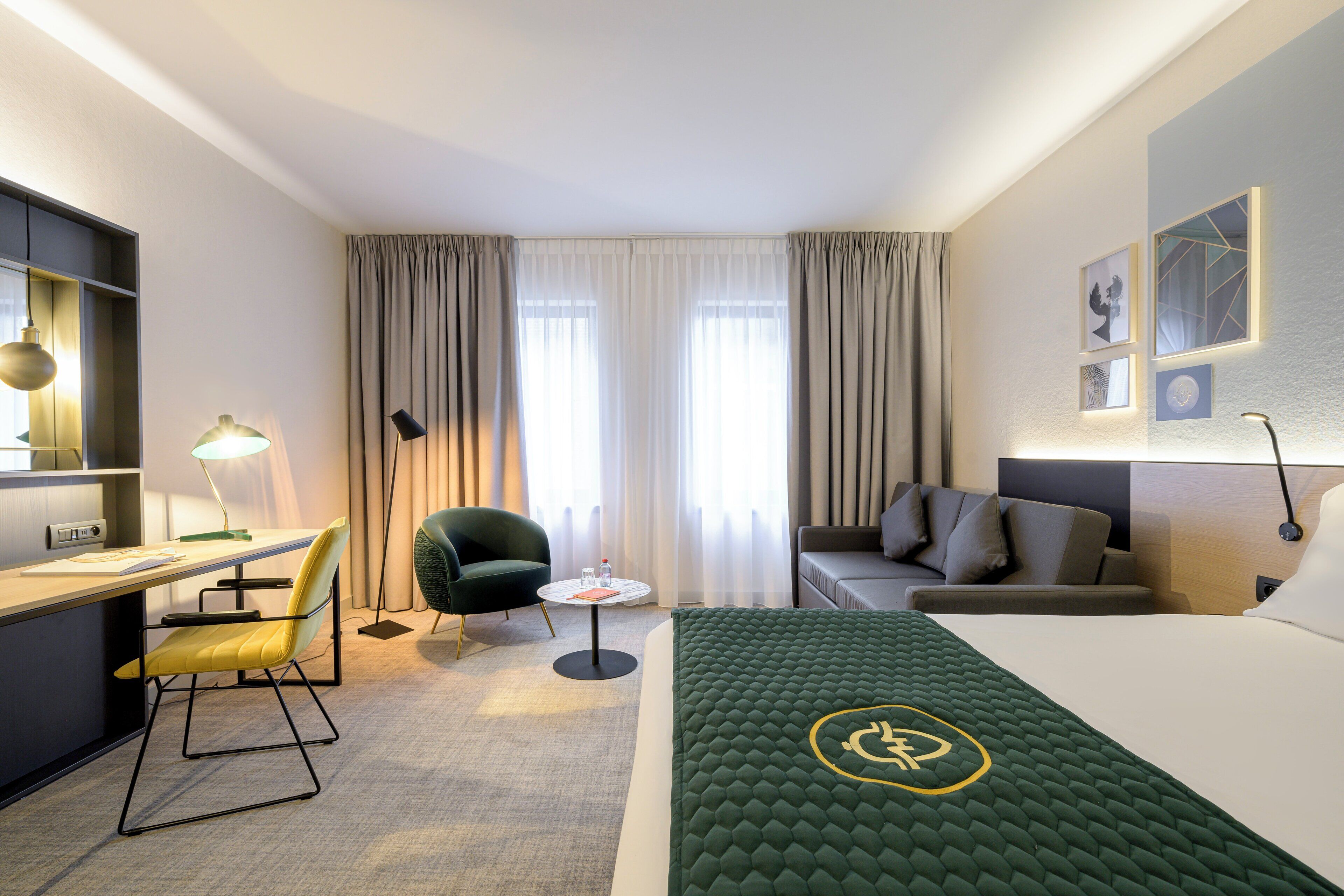 A hotel room with a bed, a desk, a chair, a sofa, and a small table.
