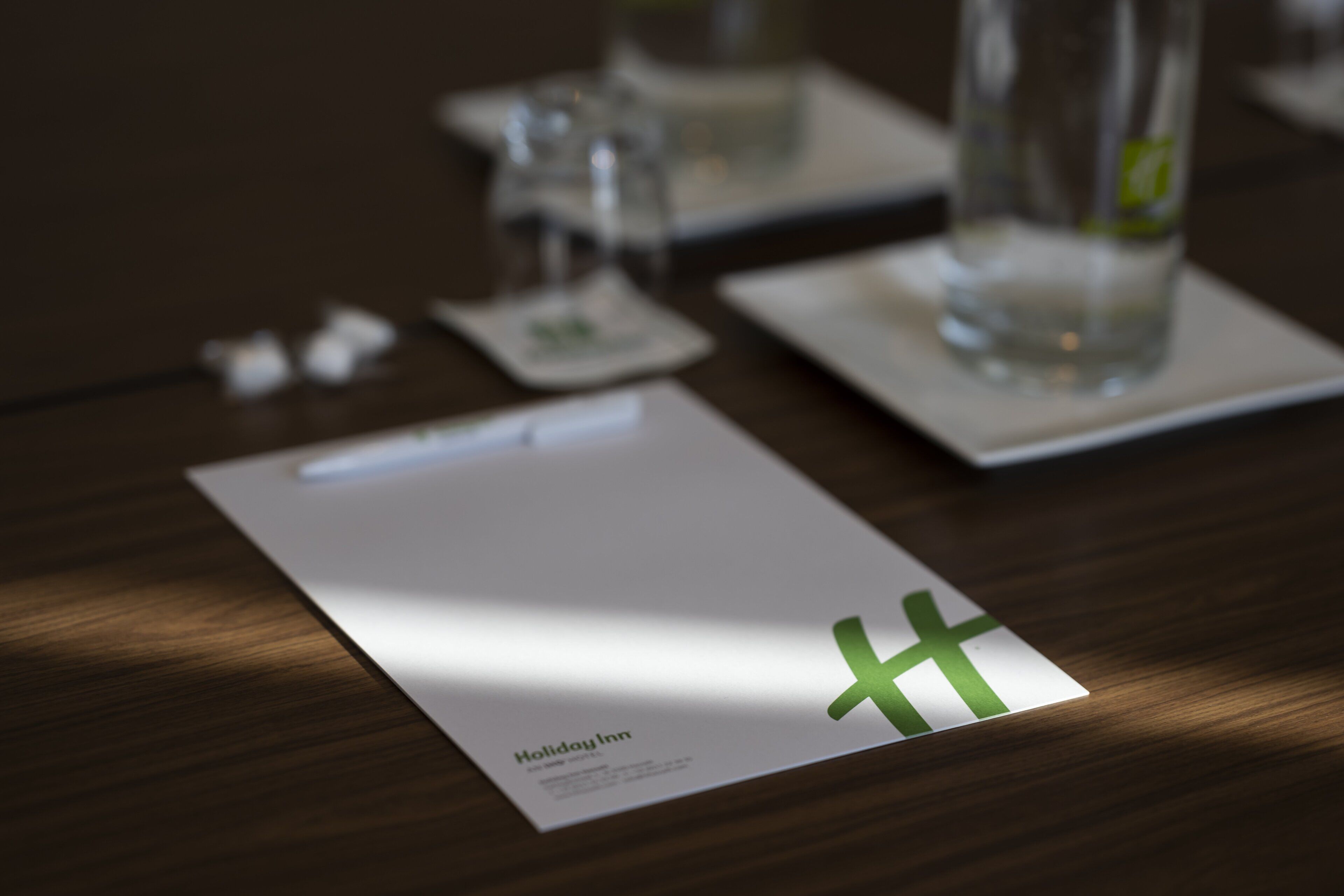 Une chambre d’hôtel avec une table en bois, un verre d’eau et une carte blanche ornée d’une croix verte.