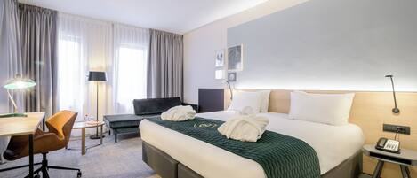 Habitación de hotel con una cama grande, un escritorio, una silla, una lámpara y un teléfono en una mesita de noche.