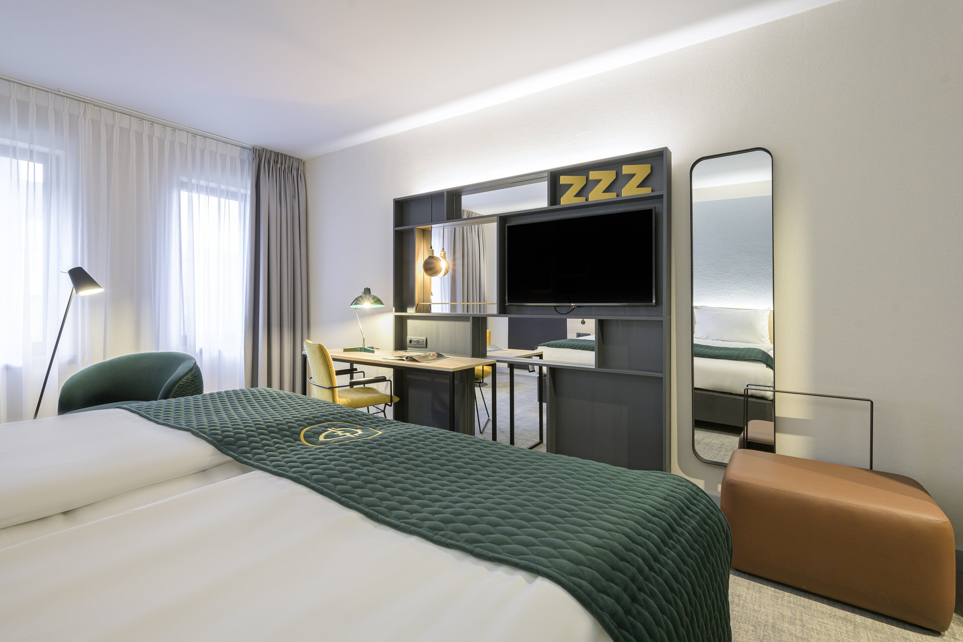 Habitación de hotel con cama, escritorio, silla, televisión y espejo.