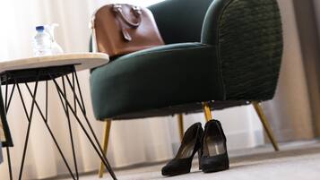 Un fauteuil vert avec un sac à main marron posé dessus, une paire d’escarpins noirs et une bouteille d’eau sur une petite table.