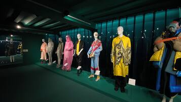 Poppen etaleren verschillende outfits in een schemerige ruimte met een groene vloer en een reflecterende muur.
