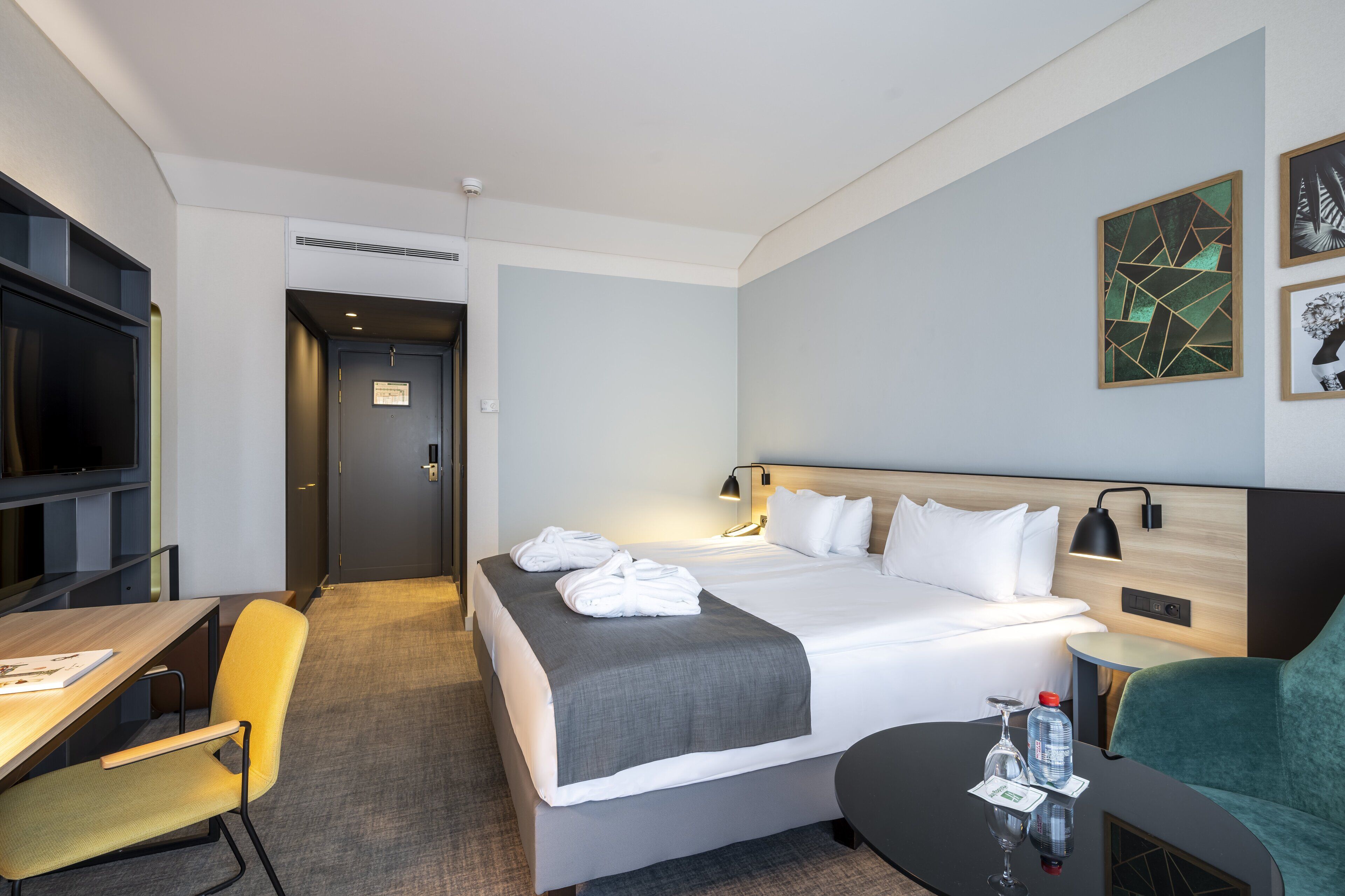 Ett hotellrum med en säng, ett nattduksbord, en stol, ett skrivbord och en tv.