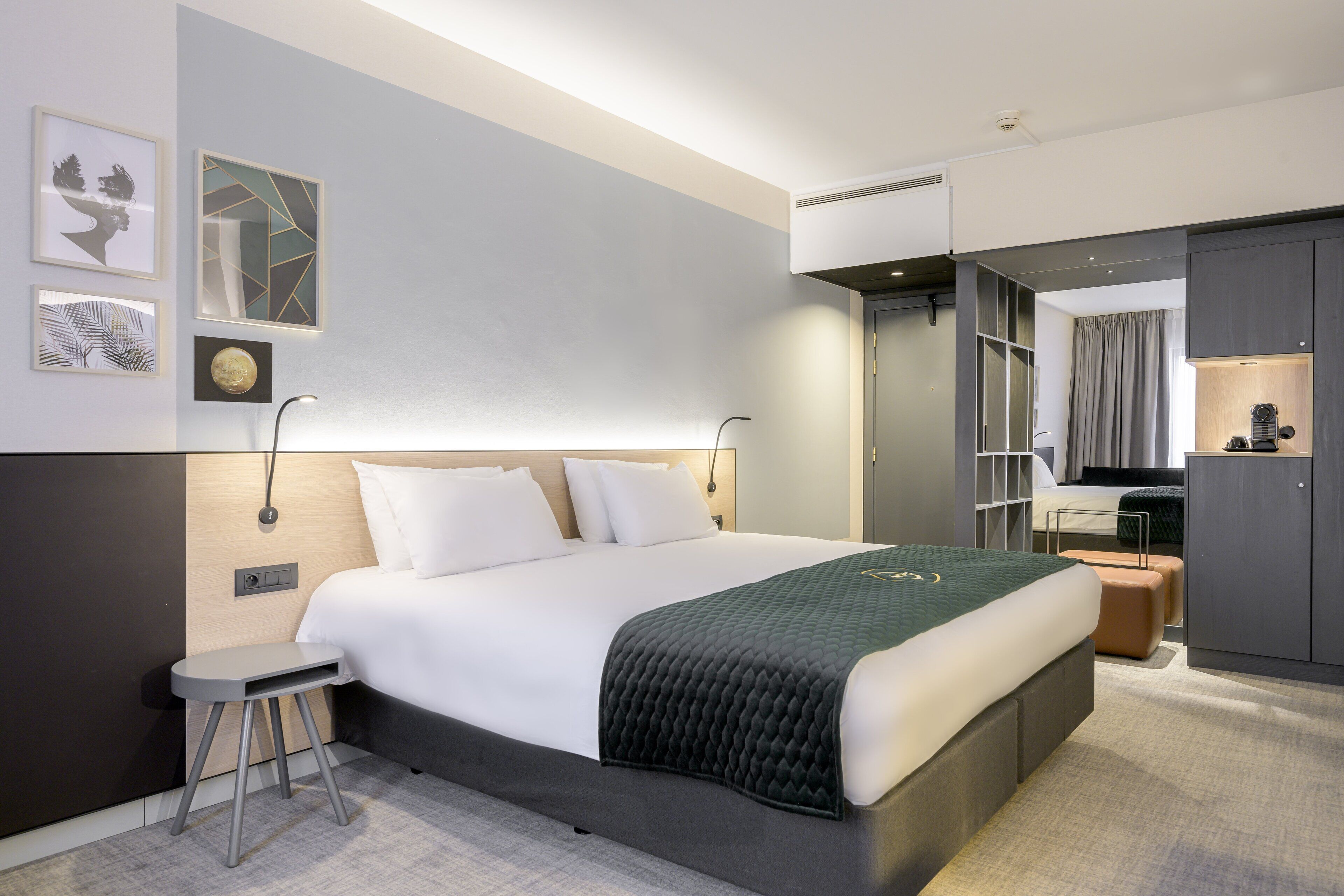 Una habitación de hotel moderna con una cama grande, mesitas de noche, un armario y un baño visible a través de una puerta abierta.