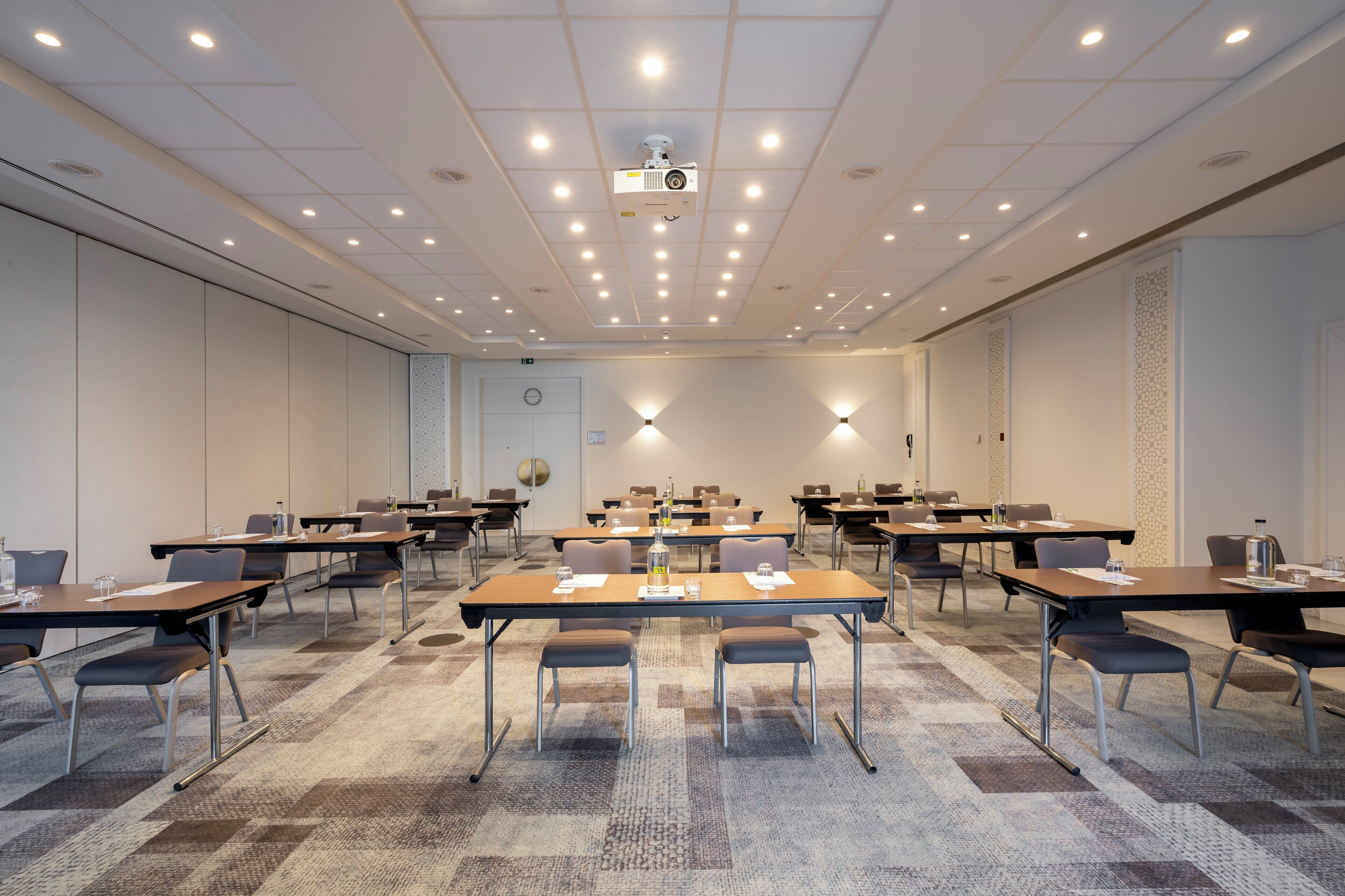 Une salle de conférence équipée de plusieurs tables, de chaises et d’un projecteur fixé au plafond.
