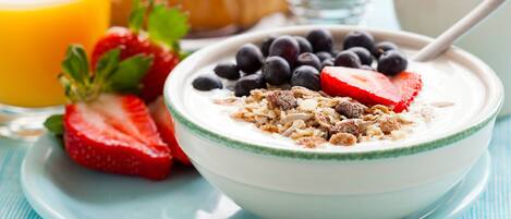 A bowl of yogurt with blueberries and strawberries, a croissant, a glass of orange juice, and a cup of coffee on a blue tablecloth.