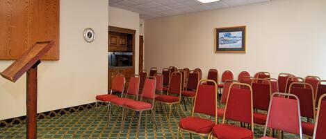 Un salón de conferencias con filas de sillas rojas, un atril de madera y una alfombra estampada.