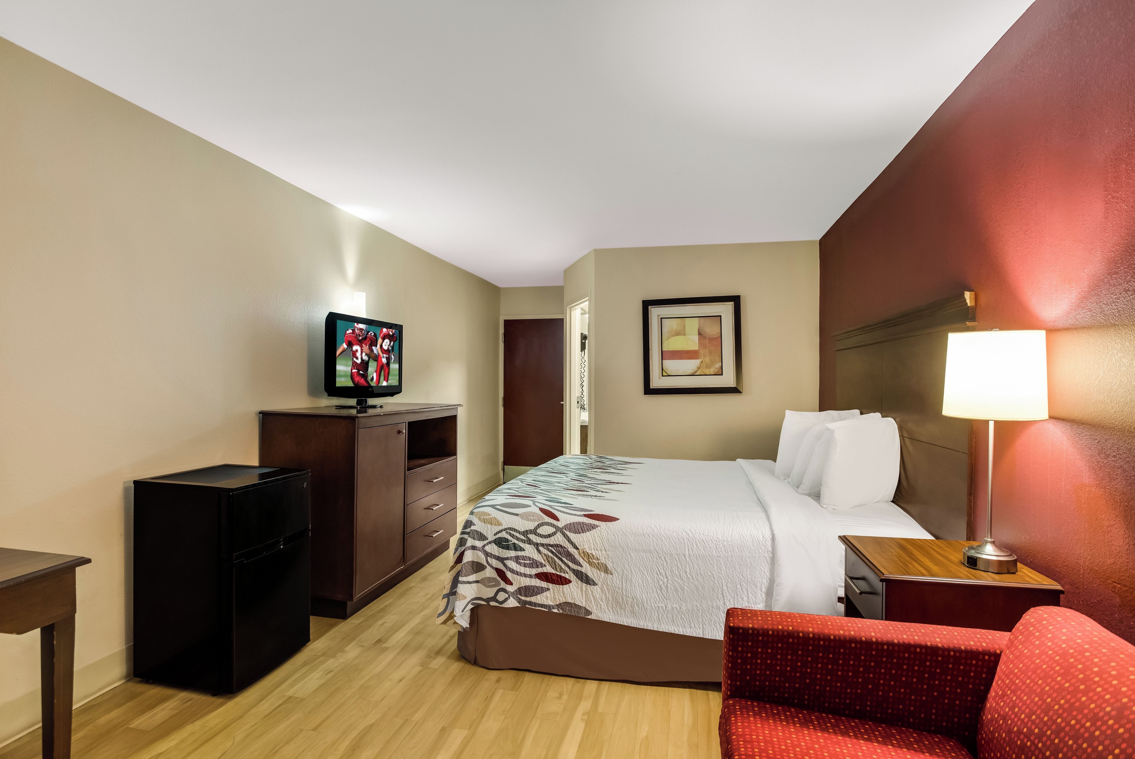 A hotel room with a bed, a desk, a television, a chair, and a lamp.