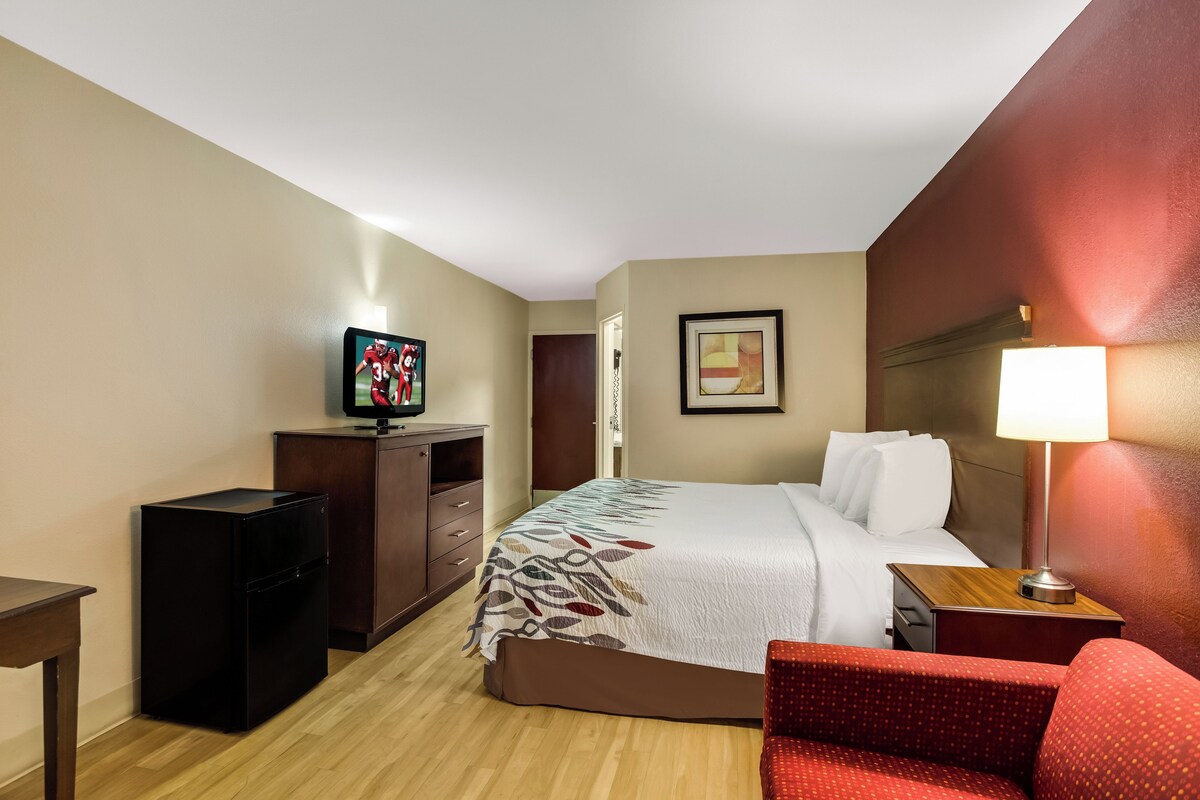 A hotel room with a bed, a desk, a television, a chair, and a lamp.
