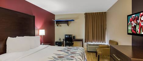 Une chambre d’hôtel avec un lit, un bureau, une chaise, une télévision et une fenêtre avec des rideaux.
