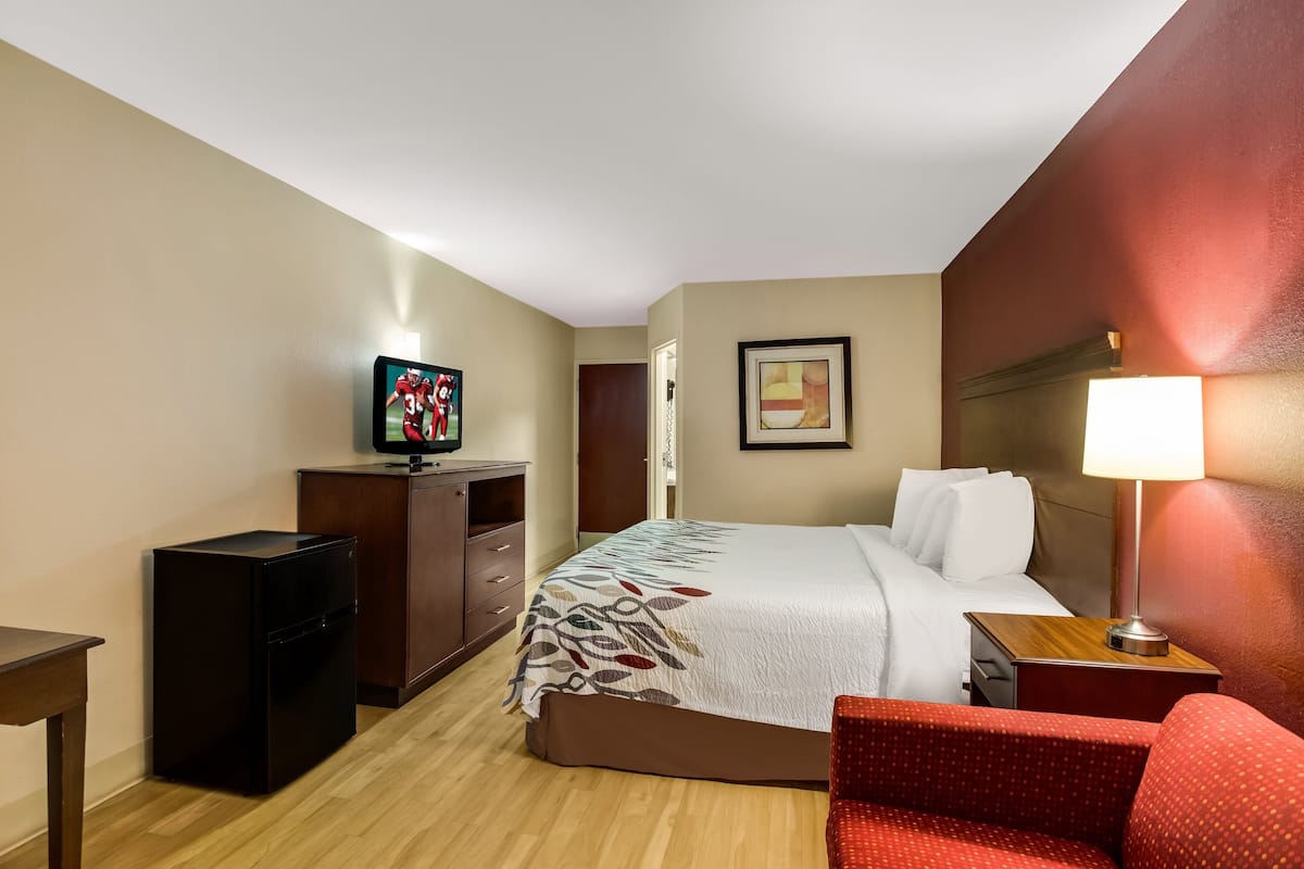 A hotel room with a bed, a television, a desk, a chair, and a nightstand with a lamp.