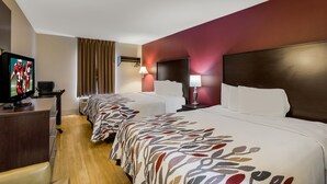 Quarto de hotel com três camas, televisão, escrivaninha e abajur.