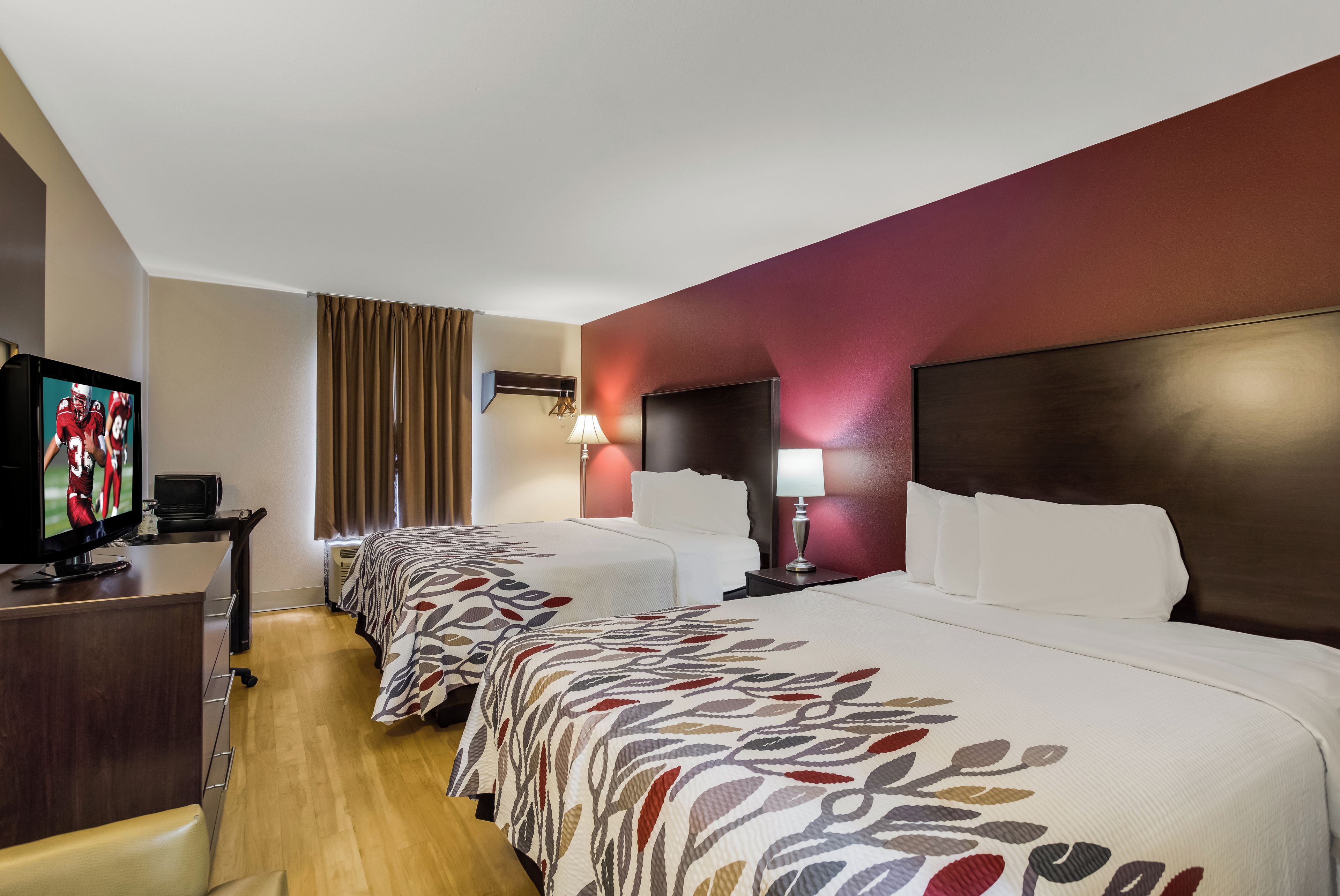 Una camera d'albergo con televisione, scrivania, lampada e un letto con copriletto a motivi.