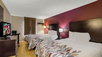 A hotel room with a television, a desk, a lamp, and a bed with a patterned bedspread.
