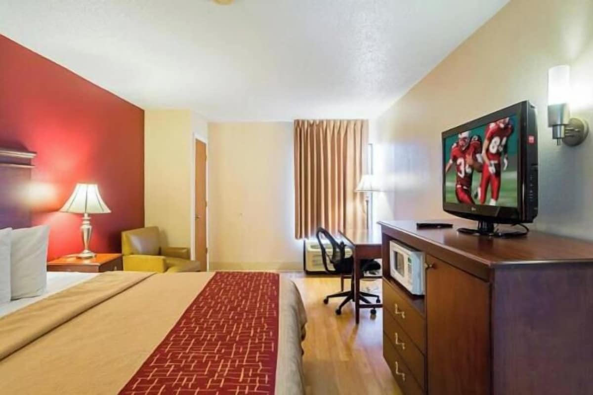 A hotel room with a bed, a desk, a television, and a window with curtains.