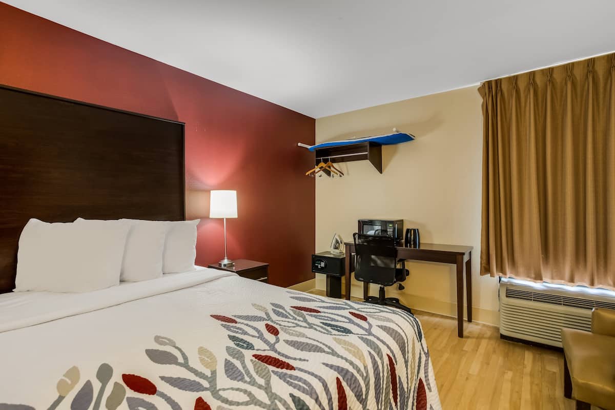 A hotel room with a bed, a desk, a chair, a microwave, and a heater.