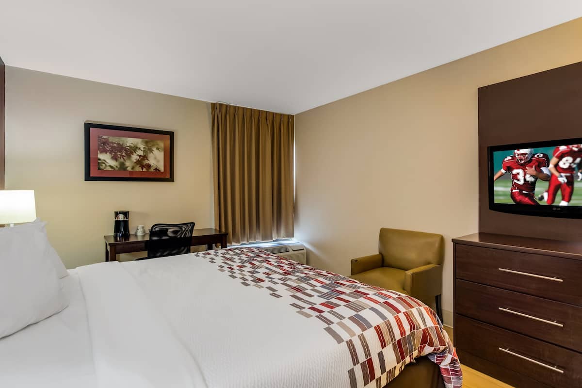 A hotel room with a bed, a desk, a chair, a TV, and a dresser.