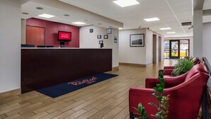 Uma área de recepção com piso de madeira, cadeiras vermelhas, balcão de recepção e sinalização indicando WiFi gratuito.