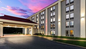 Ein modernes Hotel mit überdachter Eingangsparte, zahlreichen Fenstern und einem Parkplatz.
