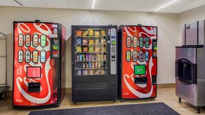 Três máquinas de venda automática com marca Coca-Cola, variedade de lanches e máquina de gelo com marca Coca-Cola.
