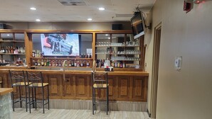 Zona de bar con mostradores de madera, taburetes y estanterías llenas de botellas y vasos.