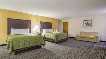 A hotel room with two beds, a sofa, a lamp, and a framed picture on the wall.