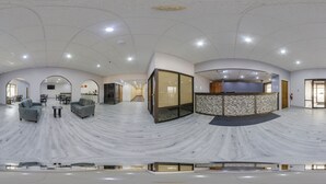 Un vestíbulo amplio con suelo ondulado, zona de estar, mostrador de recepción y puertas de vidrio que dan a otras salas.