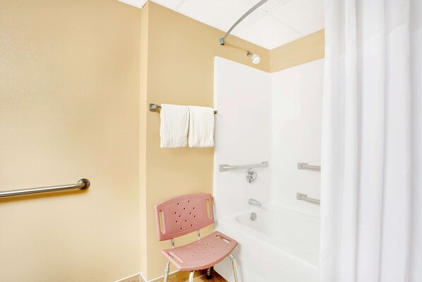 Un baño con bañera, ducha, una silla rosa y una barra de apoyo.