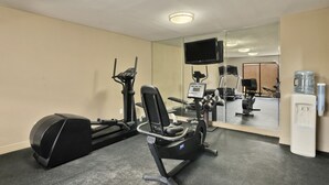 Een sportschool met trainingsapparatuur, een waterdispenser en een televisie aan de muur.