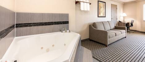A modern bathroom with a large bathtub, a sofa, and a small table with a lamp.