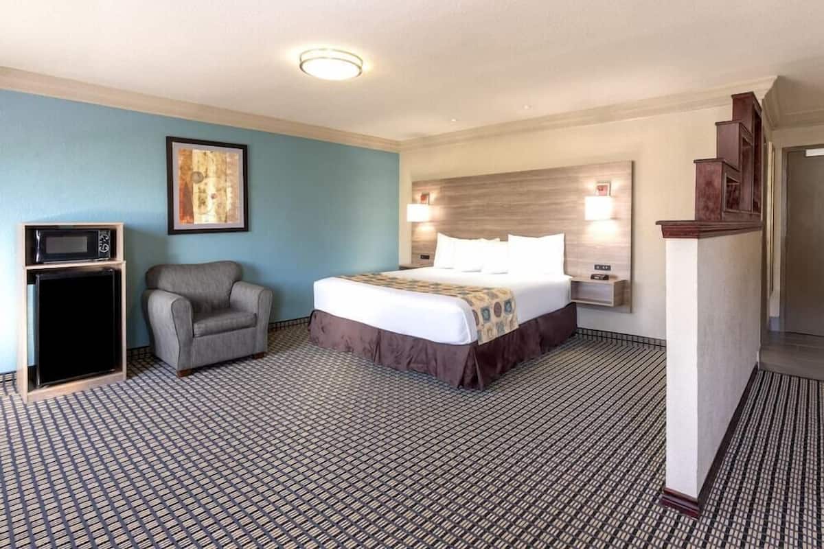 A hotel room with a bed, a chair, a microwave, a framed picture, and a staircase.