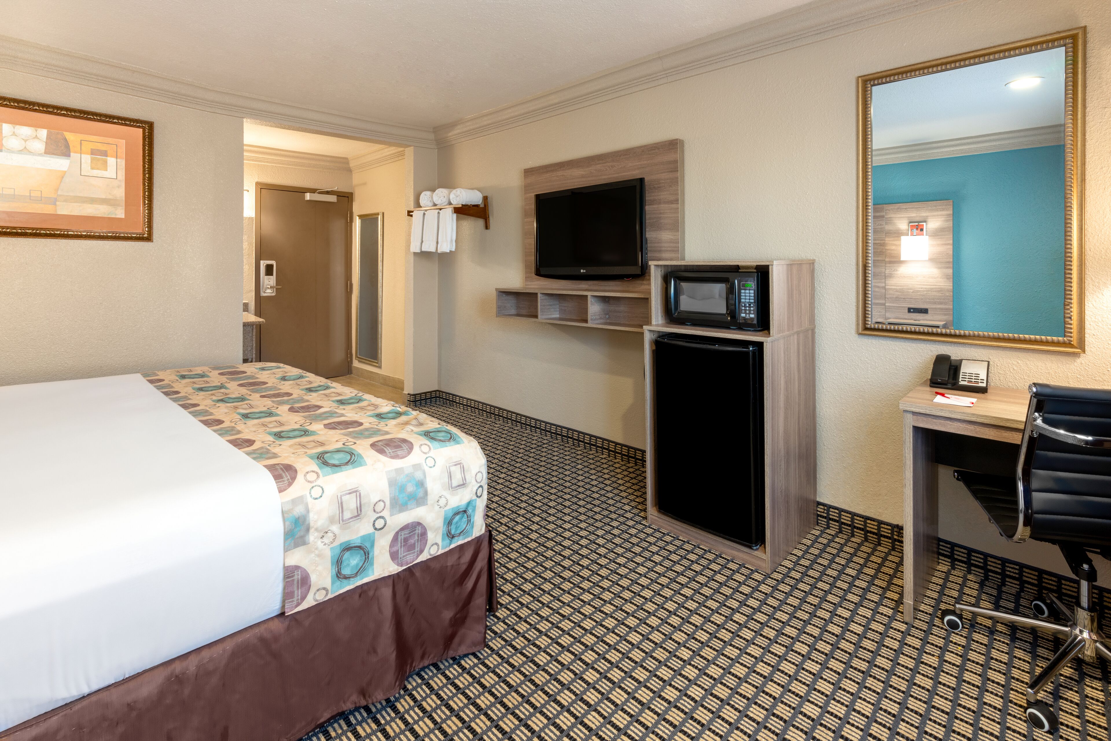 Une chambre d’hôtel équipée d’un lit, d’un bureau avec une chaise, d’une télévision, d’un four à micro-ondes et d’un miroir.
