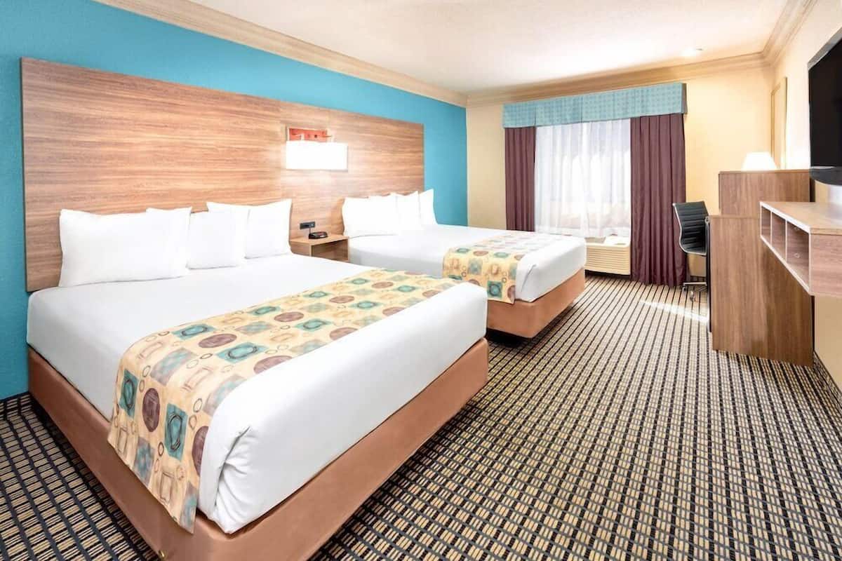 A hotel room with two beds, a desk, a TV, and a window with curtains.