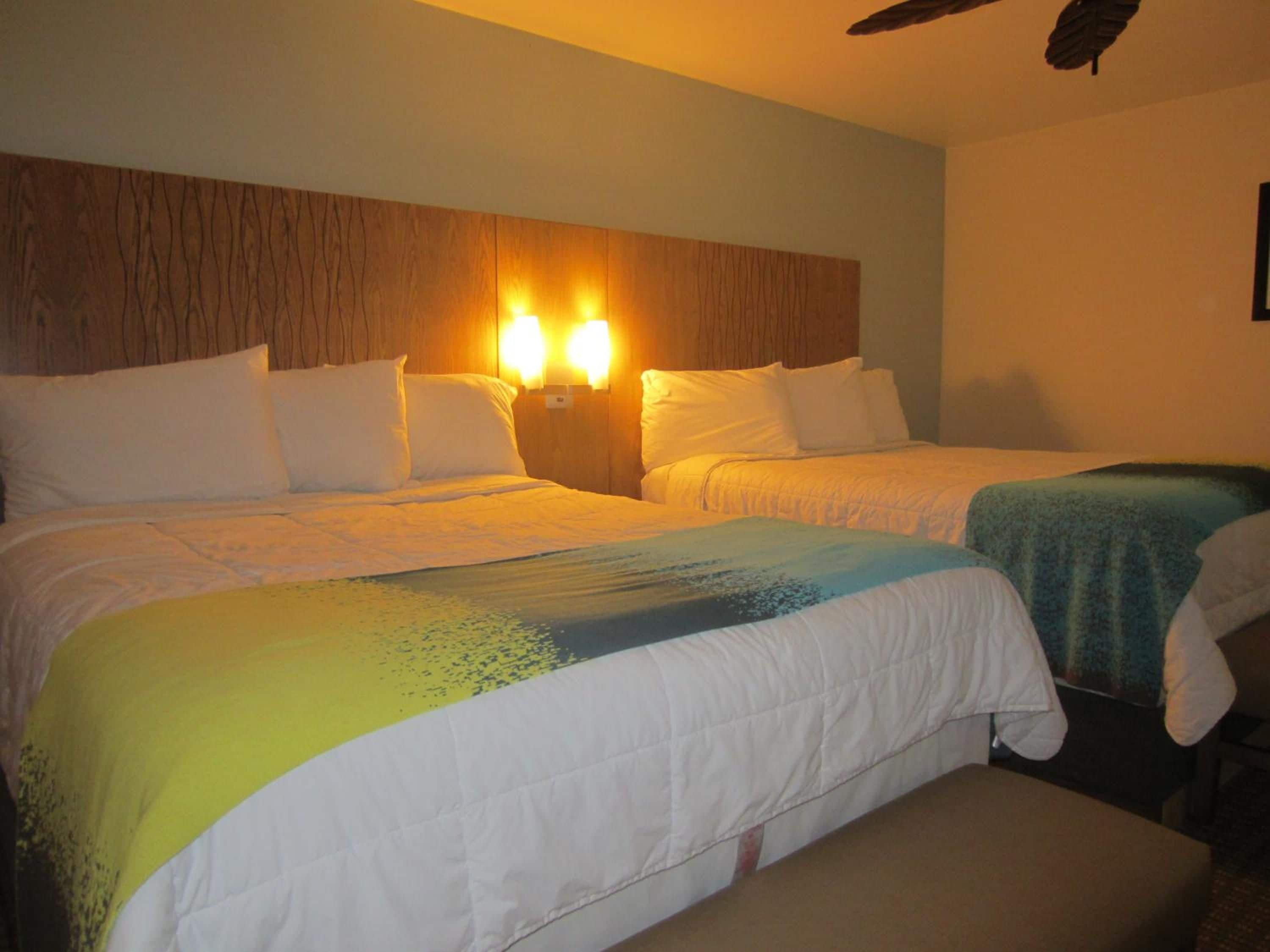 A hotel room with two beds, a wooden headboard, and wall-mounted lights.