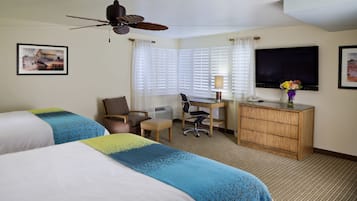 A hotel room with two beds, a desk, a television, and a ceiling fan.