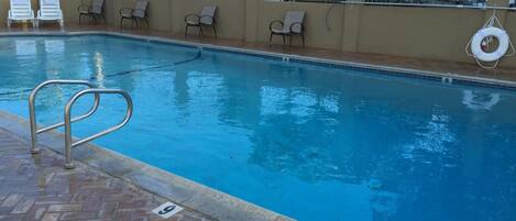 A swimming pool with a tiled deck, lounge chairs, and a fence with a gate.