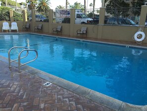 Una piscina con borde de baldosas, sillas de descanso y una cerca con portón.
