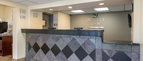 A reception desk with a tiled wall and a sign reading "Quality Inn by Choice Hotels".