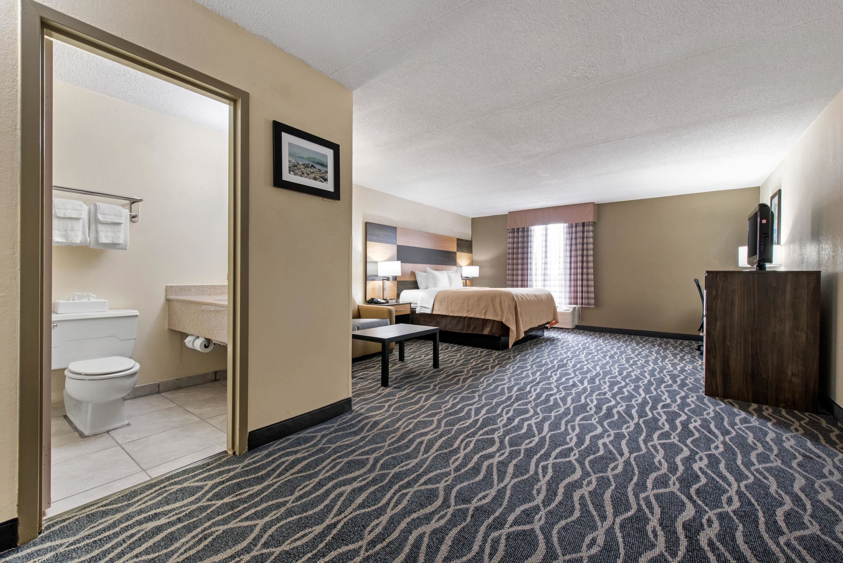 A hotel room with a bathroom, a bed, a desk, and a TV.