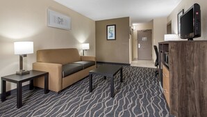 Une chambre d’hôtel avec un canapé, une petite table, une lampe, une télévision et un tapis à motifs.