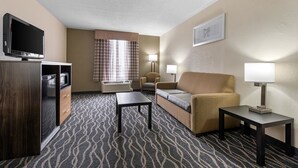 Une chambre d’hôtel avec un canapé, deux fauteuils, une télévision, un bureau et une moquette à motifs.
