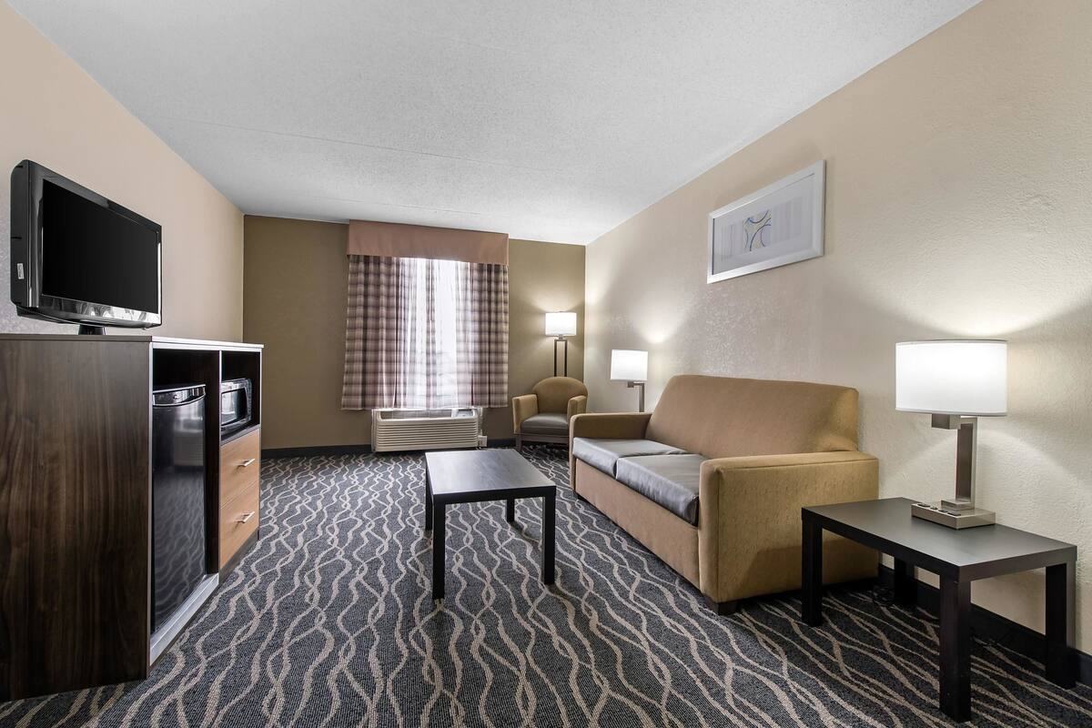 A hotel room with a sofa, two armchairs, a TV, a desk, and a patterned carpet.